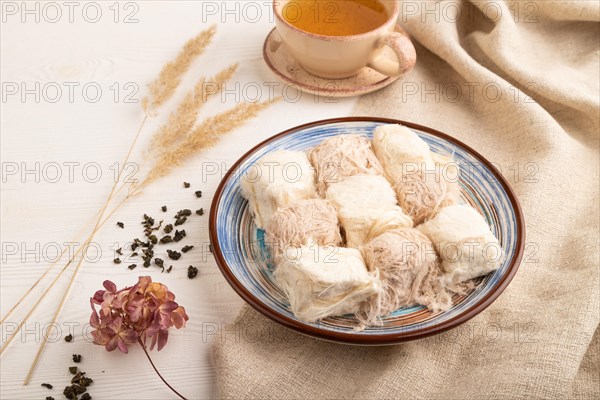 Traditional arabic sweets pishmanie and a cup of green tea on white wooden background and linen textile. side view, close up
