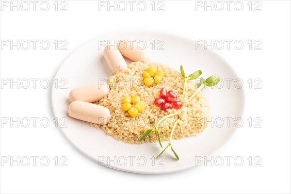 Funny mixed quinoa porridge, sweet corn, pomegranate seeds and small sausages in form of cat face isolated on white background. Side view, close up. Food for children, healthy food concept
