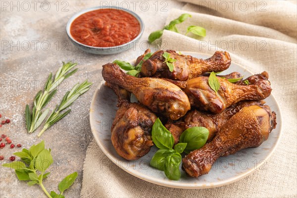 Smoked chicken legs with herbs and spices on a ceramic plate with linen textile on a brown concrete background. Side view, close up