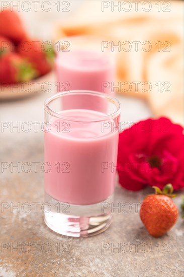 Sweet strawberry liqueur in glass on a gray concrete background and orange textile. side view, close up, selective focus