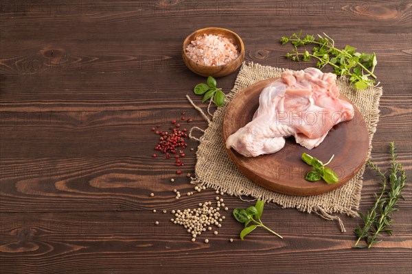 Raw turkey wing with herbs and spices on a wooden cutting board on a brown wooden background and linen textile. Side view, copy space