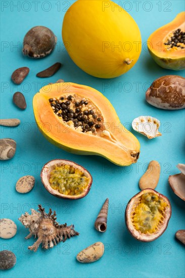Ripe cut papaya, melon, passion fruit, seashells, pebbles on blue pastel background. Side view, close up. Tropical, healthy food, vacation, holidays concept