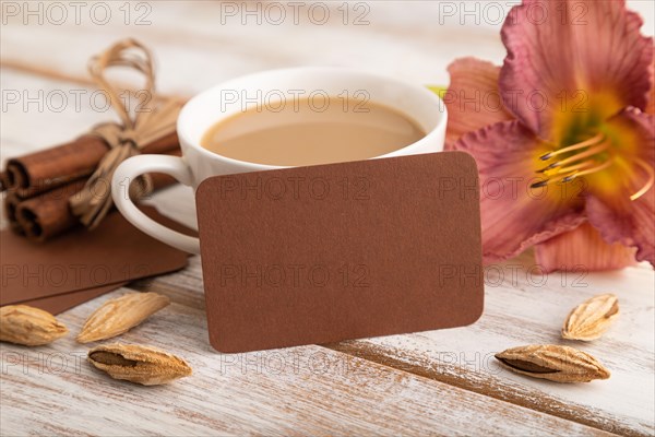 Brown paper business card mockup with purple day-lily flower and cup of coffee on white wooden background. Blank, side view, copy space, still life. spring concept