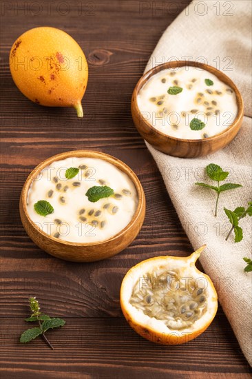 Yoghurt with granadilla and mint in wooden bowl on brown wooden background and linen textile. side view, close up