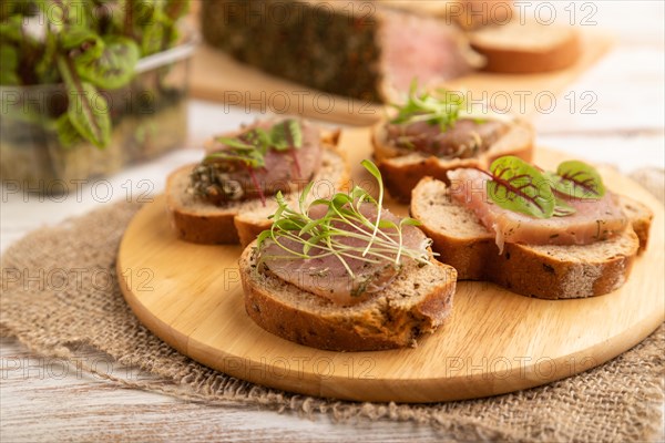 Bread sandwiches with jerky salted meat, sorrel and cilantro microgreen on white wooden background and linen textile. side view, close up, selective focus