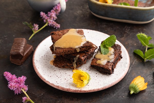 Chocolate brownie with caramel sauce with a cup of coffee on black concrete background. side view, close up