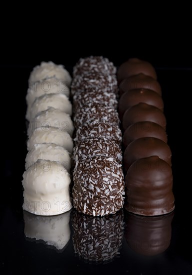 Row of chocolate kisses covered with dark and light chocolate, grated coconut, reflection, dark background