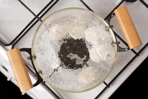 Overhead closeup view of transparent glass saucepan with boiling eggs on a gas stove