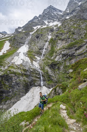 Mountaineer on a hiking trail, mountain landscape with small waterfall and rocky mountain peak, Berliner Hoehenweg, Zillertal Alps, Tyrol, Austria, Europe