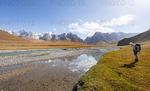 Mountaineer hiking to the mountain lake Kol Suu, mountain landscape with yellow meadows, river Kol Suu and mountain peaks with glacier, Keltan Mountains, Sary Beles Mountains, Tien Shan, Naryn Province, Kyrgyzstan, Asia