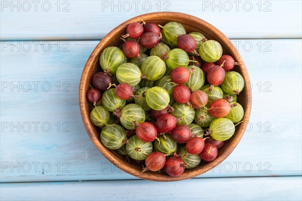 Fresh red and green gooseberry in wooden bowl on blue wooden background. top view, flat lay, close up