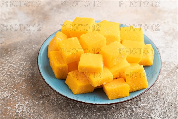 Dried and candied mango cubes on blue plate on brown concrete background. Side view, close up, vegan, vegetarian food concept
