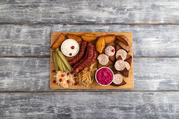Set of snacks: sausages, toast, sauerkraut, marinated onion and cucumber, baked potato on a cutting board on a gray wooden background. Top view, flat lay, close up, copy space