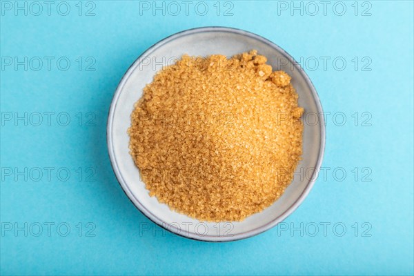 Plate with unrefined golden cane sugar on blue pastel background. top view, flat lay, close up