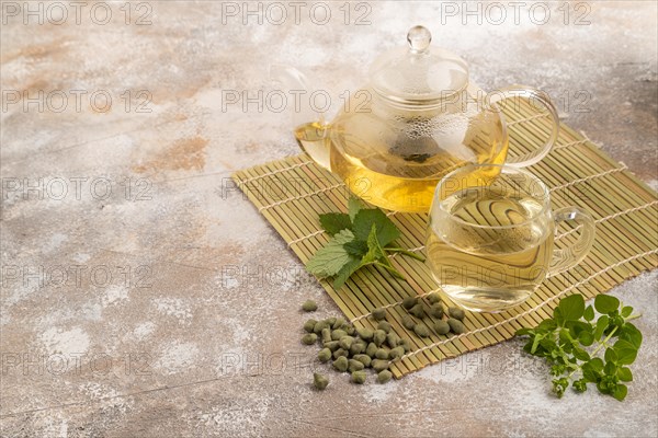 Green oolong tea with herbs in glass on brown concrete background. Healthy drink concept. Side view, copy space