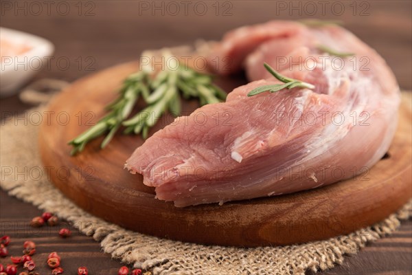 Raw pork with herbs and spices on a wooden cutting board on a brown wooden background. Side view, close up, selective focus
