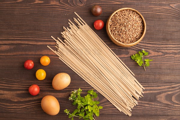 Japanese buckwheat soba noodles with tomato, eggs, spices, herbs on brown wooden background. Top view, flat lay, close up