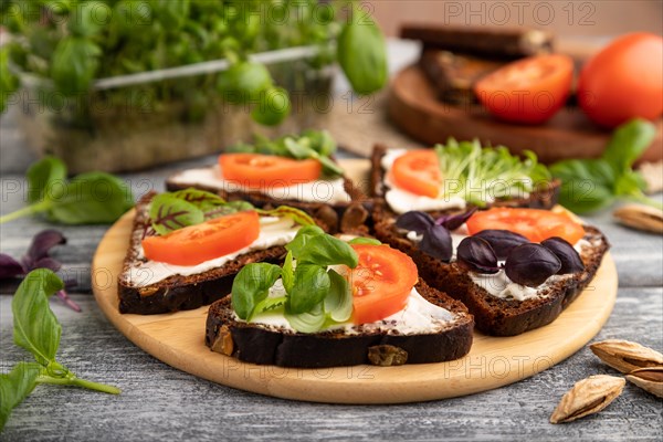 Grain rye bread sandwiches with cream cheese, tomatoes and basil microgreen on gray wooden background and linen textile. side view, close up, selective focus