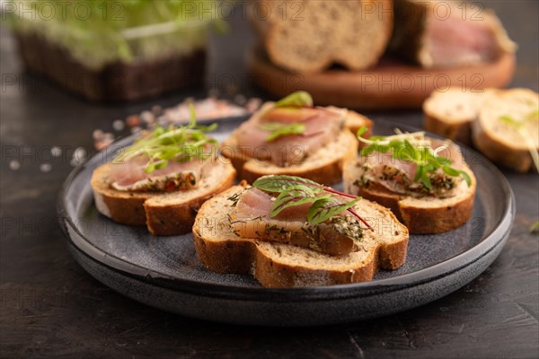 Bread sandwiches with jerky salted meat, sorrel and cilantro microgreen on black concrete background. side view, close up, selective focus