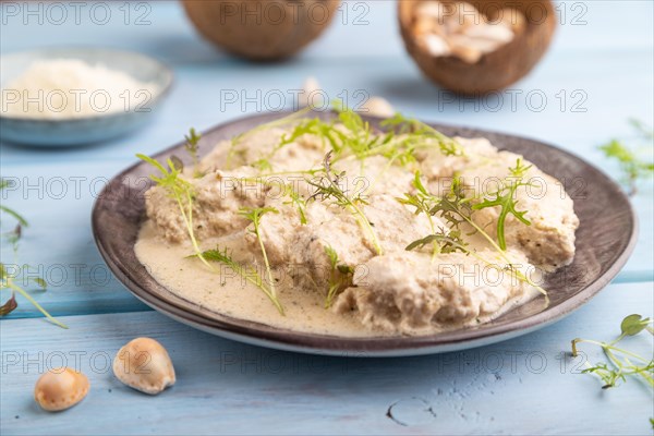 Stewed chicken fillets with coconut milk sauce and mizuna cabbage microgreen on blue wooden background. side view, close up, selective focus
