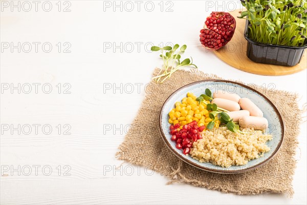 Mixed quinoa porridge, sweet corn, pomegranate seeds and small sausages on white wooden background. Side view, copy space. Food for children, healthy food concept