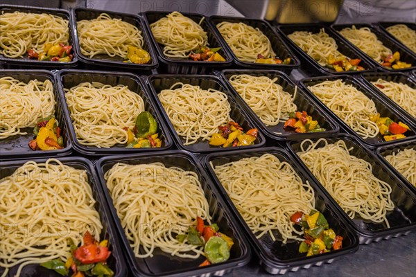 Several plastic serving containers filled with cooked spaghetti noodles and vegetables in industrial training kitchen in Singapore