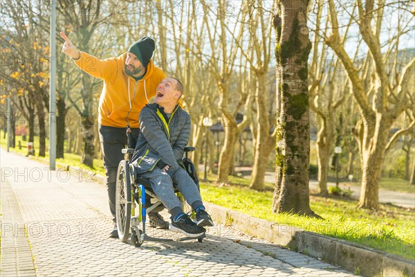 Disabled man sitting in wheelchair and friend enjoying nature pointing and looking around in a park