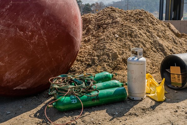 Chungju, South Korea, March 22, 2020: For editorial use only. Welding oxygen tanks and equipment laying on ground beside large metal container at construction site, Asia