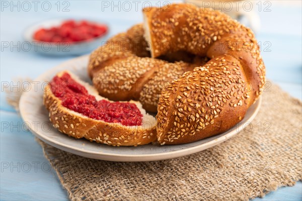 Homemade sweet bun with raspberry jam and cup of coffee on a blue wooden background and linen textile. side view, close up, selective focus