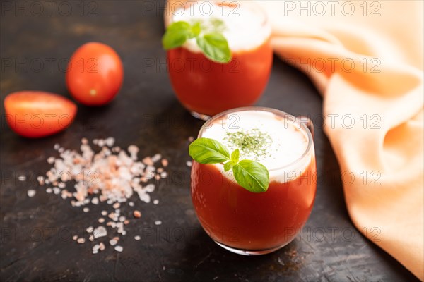 Tomato juice with basil, himalayan salt and sour cream in glass on a black concrete background with orange textile. Healthy drink concept. Side view, close up, selective focus