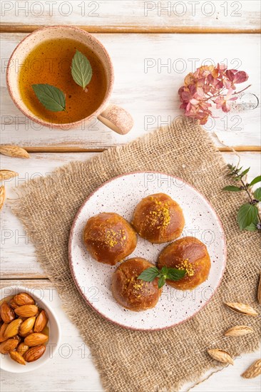 Homemade traditional turkish dessert sekerpare with almonds and honey, cup of green tea on white wooden background and linen textile. top view, flat lay