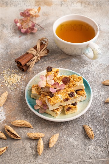 Traditional candy nougat with nuts and sesame with cup of green tea on brown concrete background. side view, close up