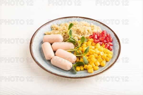 Mixed quinoa porridge, sweet corn, pomegranate seeds and small sausages on white wooden background. Side view, close up. Food for children, healthy food concept