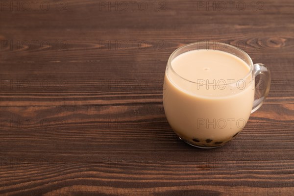 Bubble tea with pistachio and caramel in glass on brown wooden background. Healthy drink concept. Side view, copy space