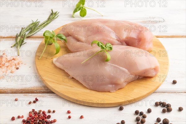 Raw chicken breast with herbs and spices on a wooden cutting board on a white wooden background. Side view, close up