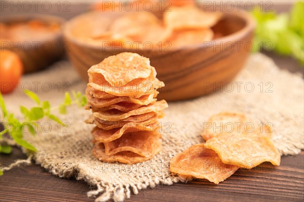 Slices of dehydrated salted meat chips with herbs and spices on brown wooden background and linen textile. Side view, close up, selective focus