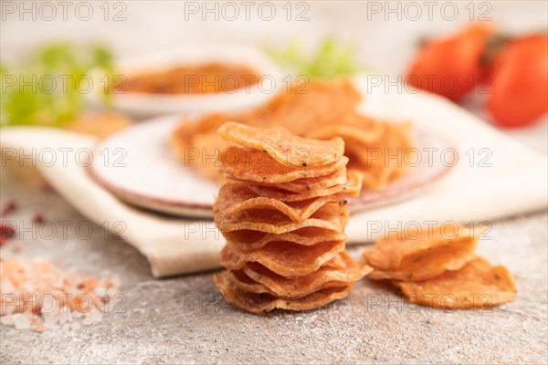 Slices of dehydrated salted meat chips with herbs and spices on gray concrete background and white textile. Side view, close up, selective focus