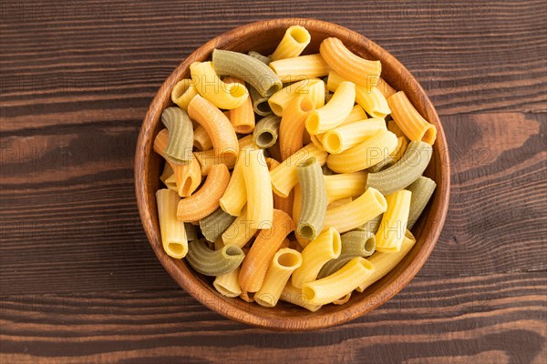 Rigatoni colored raw pasta with tomato, eggs, spices, herbs on brown wooden background. Top view, flat lay, close up