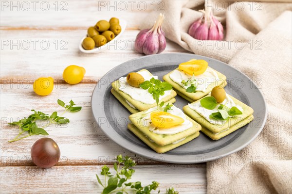 Green cracker sandwiches with cream cheese and cherry tomatoes on white wooden background and linen textile. side view, close up