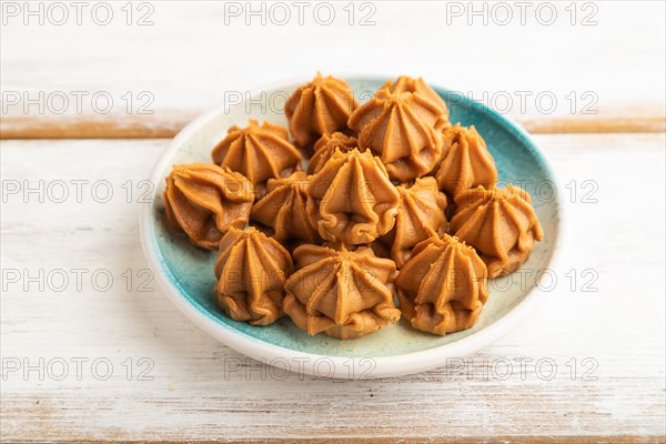 Homemade soft caramel fudge candies on blue plate on white wooden background. side view, close up