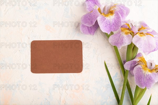 Brown business card with lilac iris flowers on white concrete background. top view, flat lay, copy space, still life. Breakfast, morning, spring concept