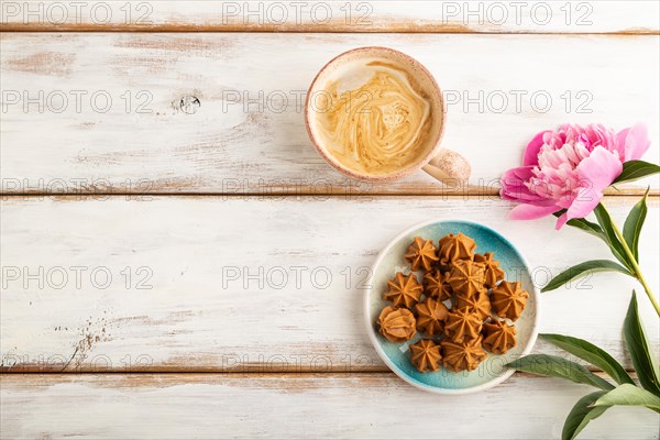 Homemade soft caramel fudge candies on blue plate and cup of coffee on white wooden background, peony flower decoration. top view, flat lay, copy space