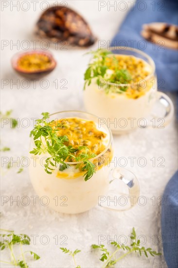 Yogurt with passionfruit and marigold microgreen in glass on gray concrete background with blue linen textile. Side view, close up, selective focus