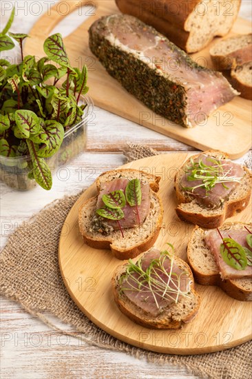 Bread sandwiches with jerky salted meat, sorrel and cilantro microgreen on white wooden background and linen textile. side view, close up