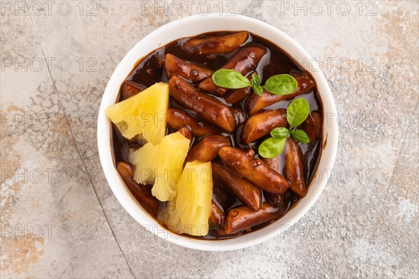 Tteokbokki or Topokki, fried rice cake stick, popular Korean street food with spicy jjajang sauce and pineapple on gray concrete background. Top view, flat lay