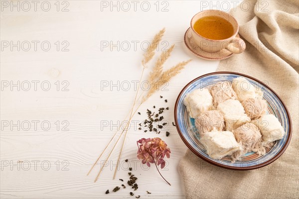 Traditional arabic sweets pishmanie and a cup of green tea on white wooden background and linen textile. side view, copy space