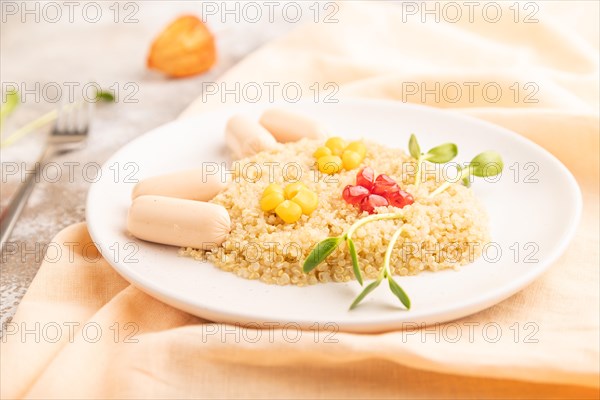 Funny mixed quinoa porridge, sweet corn, pomegranate seeds and small sausages in form of cat face on brown concrete background and orange textile. Side view, selective focus, food for children, healthy food concept