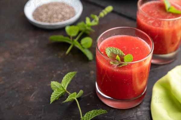 Watermelon juice with chia seeds and mint in glass on a black concrete background with green textile. Healthy drink concept. Side view, close up, selective focus