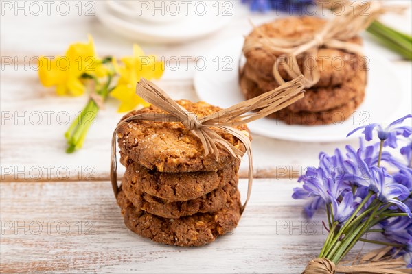 Oatmeal cookies with spring snowdrop flowers bluebells, narcissus and cup of coffee on white wooden background. side view, close up, still life. Breakfast, morning, spring concept
