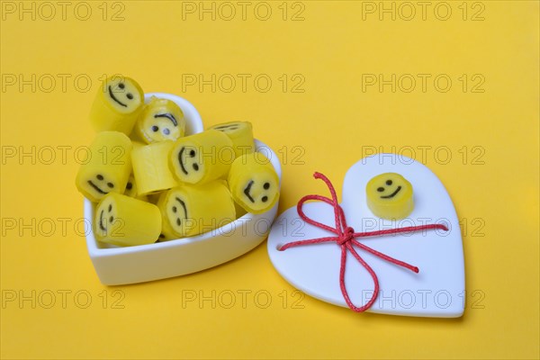 Yellow sweets with smiley in a heart-shaped bowl